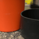 Orange tumbler beside a black silicone boot, showing the dirt ring a boot can leave on a countertop
