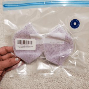Two lavender glitter silicone tumbler boots packaged in a clear resealable bag, held in hand