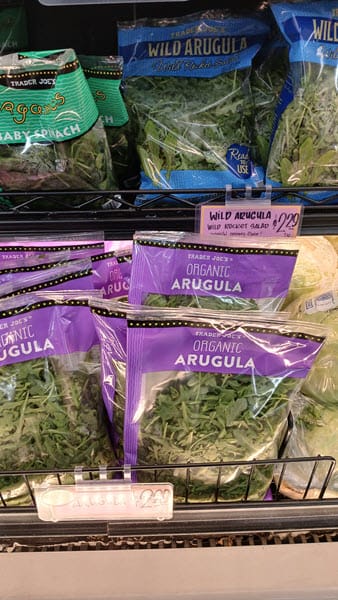 Bags of Trader Joe&rsquo;s Organic Arugula on a store shelf with a $2.29 price tag