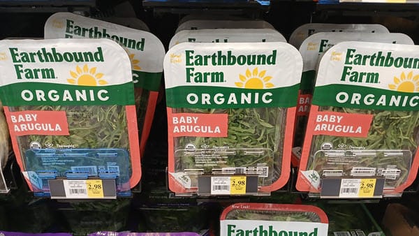 Clamshells of Earthbound Farm Organic Baby Arugula on a store shelf priced at $2.98