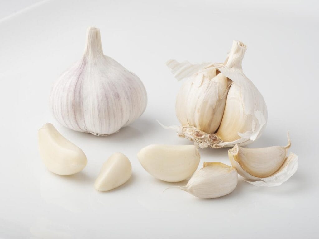 A whole garlic bulb, a split bulb, and loose peeled and unpeeled cloves on a white surface