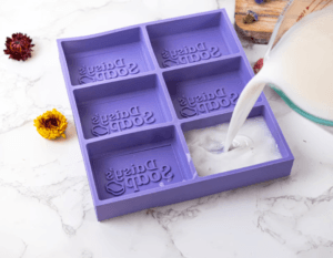 Purple silicone six-cavity soap mold that embosses ‘Daily Soap’ into each bar, with soap batter being poured in
