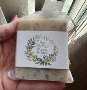 Handmade soap in an organza bag with a floral ‘From Shelby’s Shower to Yours’ favor label, held in hand