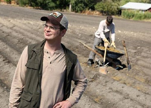 Scene from The Office of Dwight Schrute standing in a field at his beet farm while a worker shovels behind him